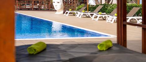 A pool area with lounge chairs and umbrellas, a white sculpture, and a view of buildings in the background.
