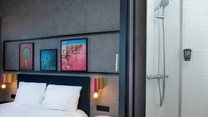 Una habitación de hotel moderna con cama, cuadros enmarcados, ducha y luz empotrada en la pared.