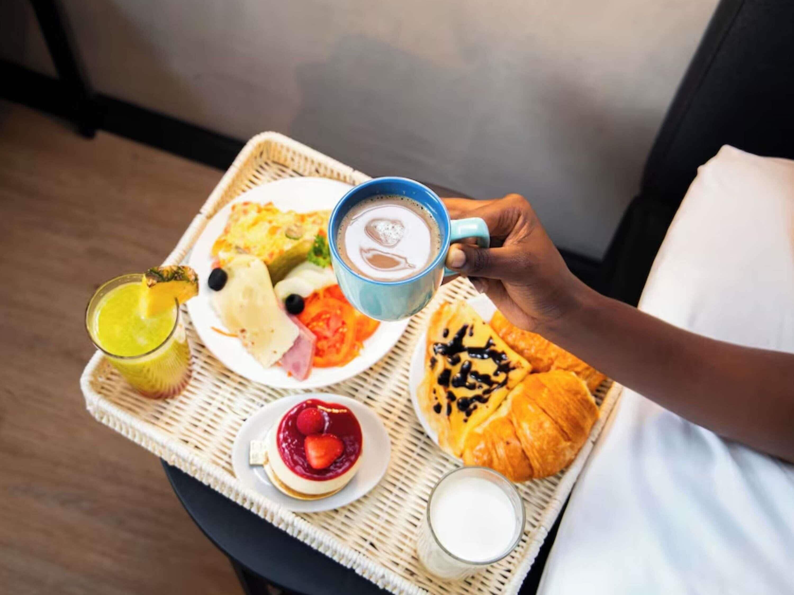 Een dienblad met ontbijtartikelen, waaronder croissants, een bord eten, een glas sap, een kop koffie en een glas melk.