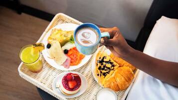 Een dienblad met ontbijtartikelen, waaronder croissants, een bord eten, een glas sap, een kop koffie en een glas melk.