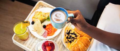 Un vassoio con prodotti per la colazione, tra cui croissant, un piatto di cibo, un bicchiere di succo, una tazza di caffè e un bicchiere di latte.