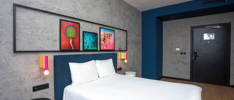 A modern hotel room with a large bed, a headboard, and artwork on the wall.