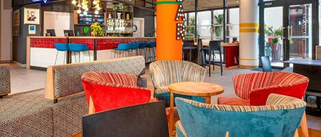 Un'area bar moderna con insegna al neon, sedute colorate e un bancone bar con diversi tipi di bottiglie.