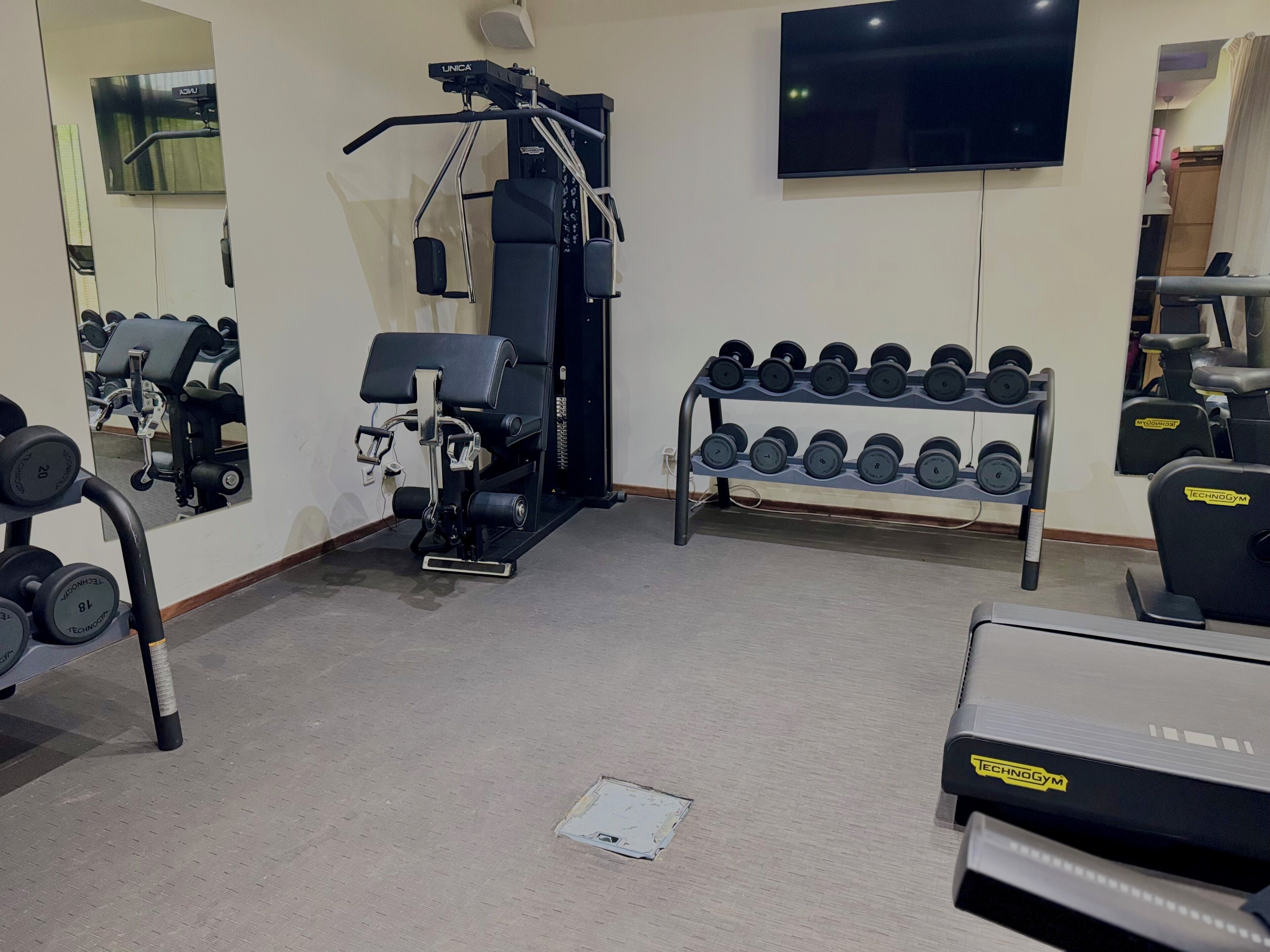 Un gimnasio con equipo de ejercicio, un televisor y un estante con mancuernas.