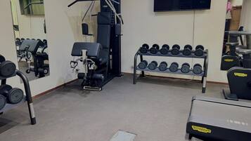A gym with exercise equipment, a TV, and a rack of dumbbells.