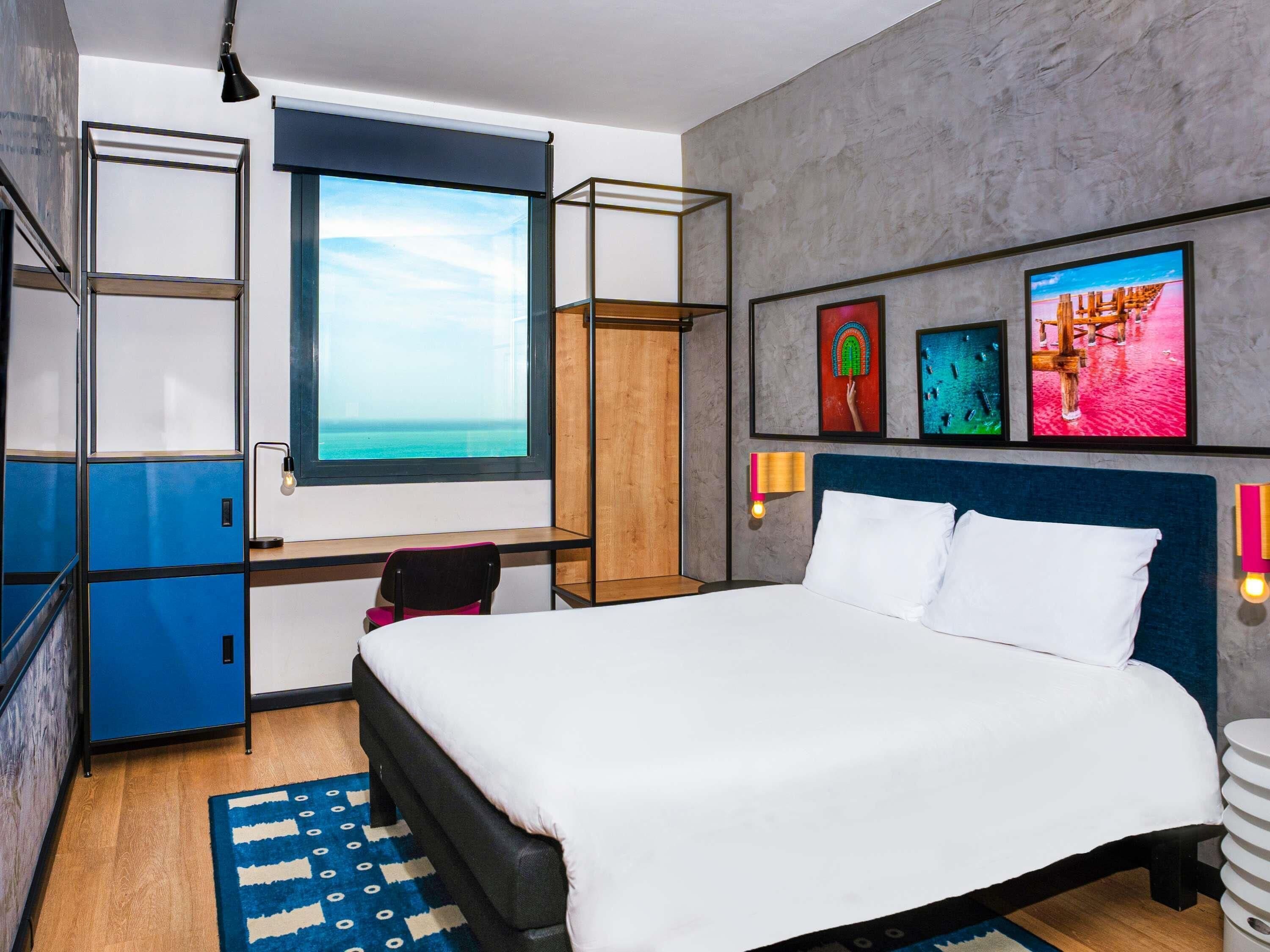 A modern bedroom with a large bed, a desk, and a view of the ocean.