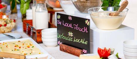 Una mesa de buffet con diversos alimentos, un letrero que dice 'Local Touch' y una tabla de madera con queso y tomates.