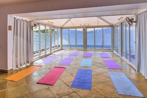 A spacious room with large windows, multiple yoga mats, and a fan.