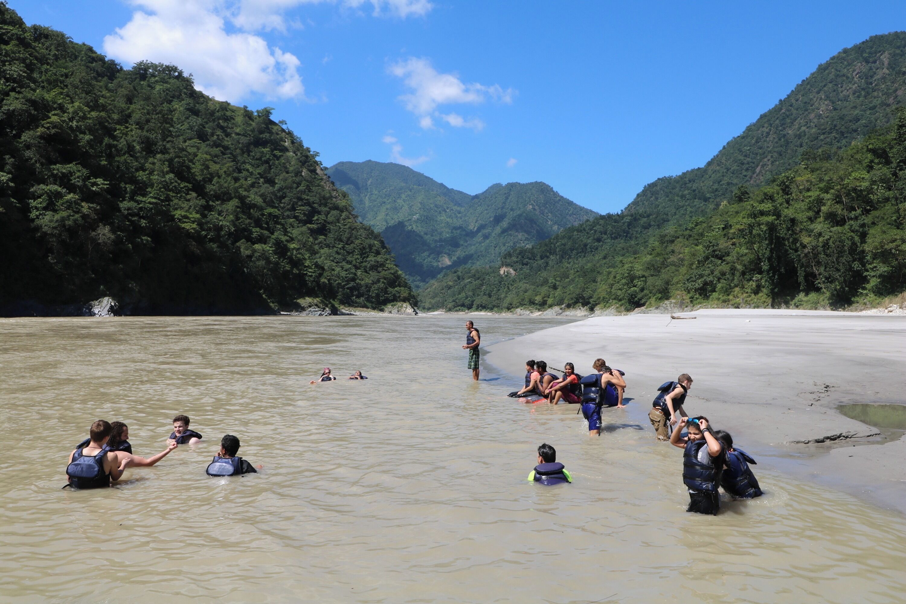 Un groupe de personnes se trouve dans une rivière, entouré de collines verdoyantes.