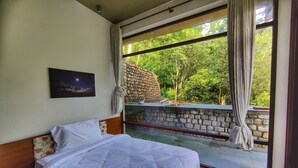 A bedroom with a large window, a bed, a night sky picture, and a stone wall outside.