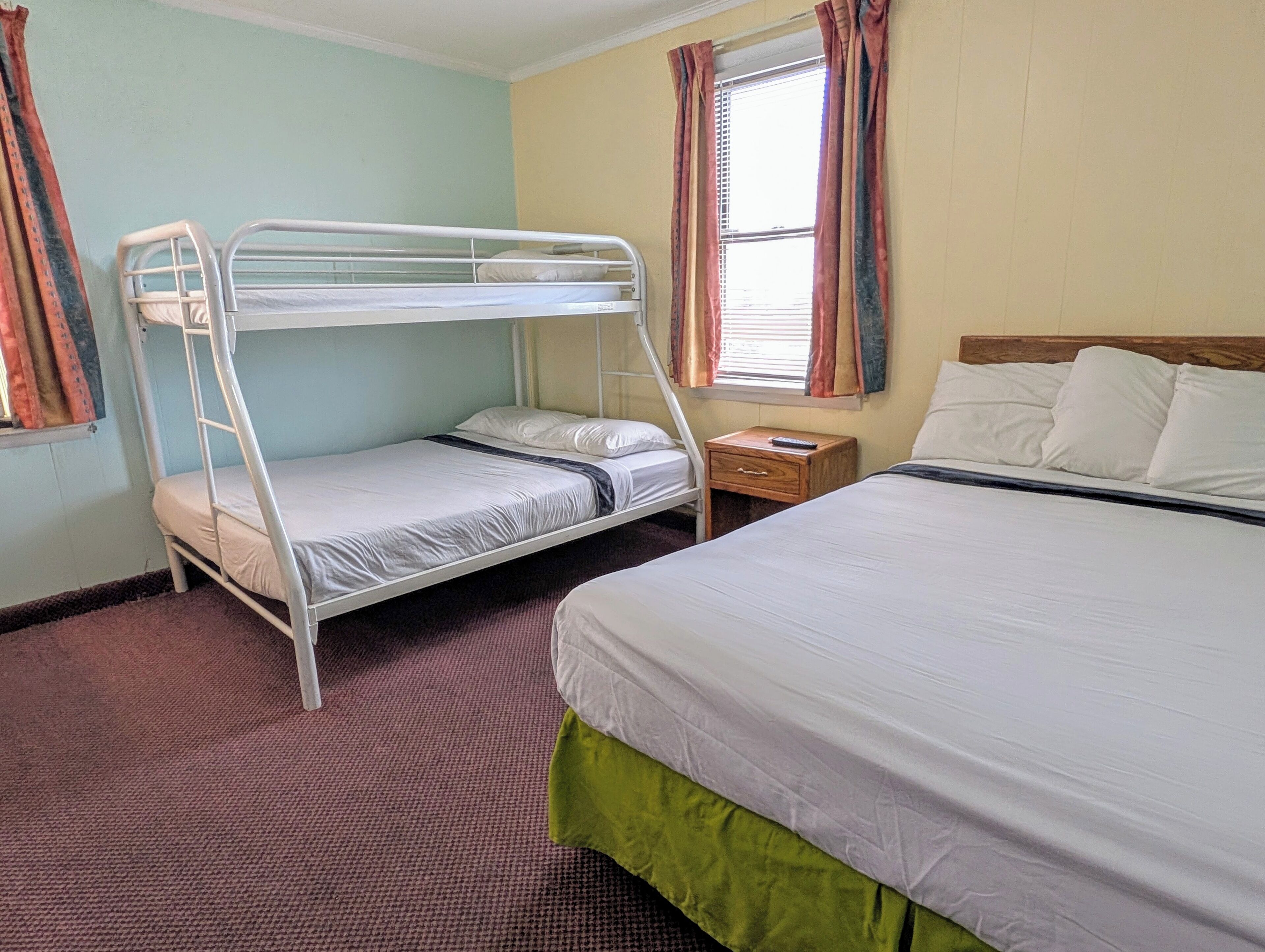 Quarto com beliches, uma cama de solteiro, mesa de cabeceira e janela com cortinas.