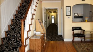A staircase with patterned carpet, a wooden bench with magazines, a hallway with patterned carpet, a black leather chair, and a clock on the wall.