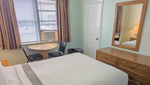 A hotel room with a bed, a wooden dresser, a round table, and a chair.