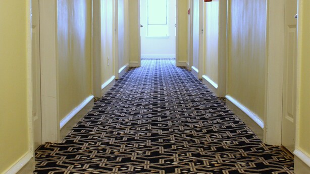 A hallway with patterned carpet, white walls, and a ceiling fan.