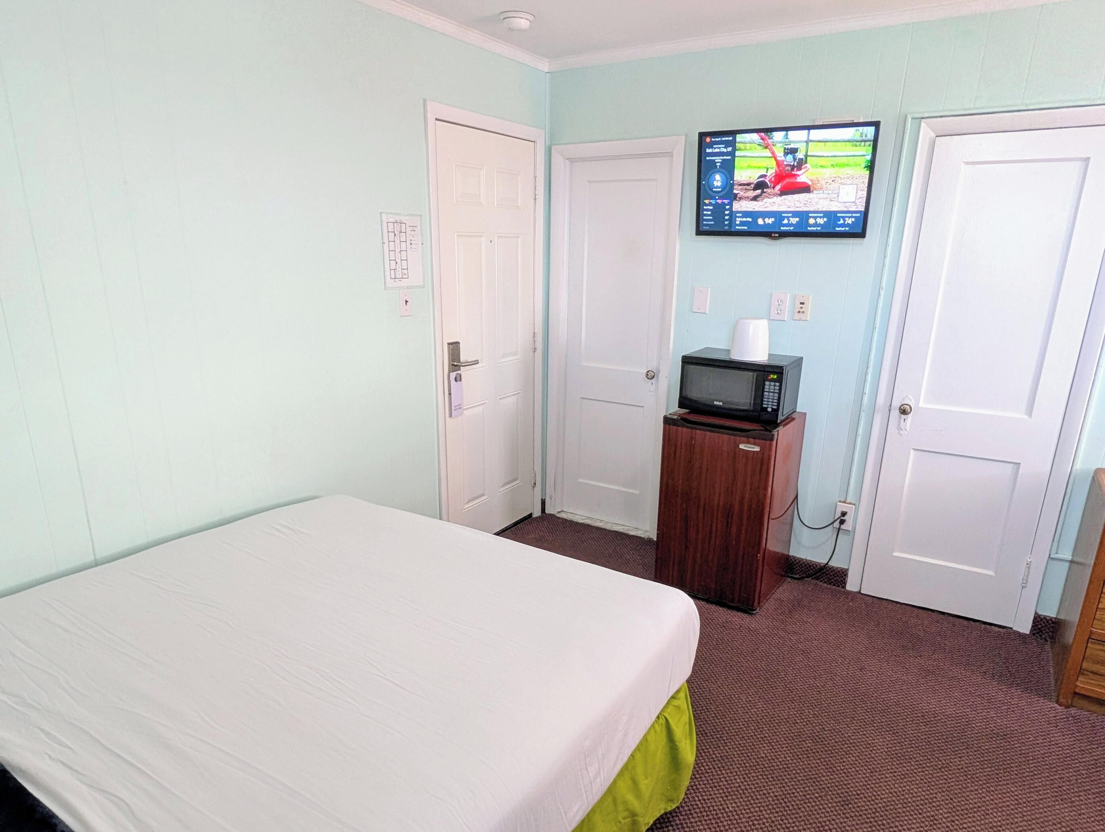Een kamer met een bed, een aan de muur bevestigde televisie en een magnetron op een kastje.