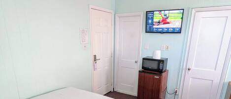 A room with a bed, a television mounted on the wall, and a microwave on a small cabinet.