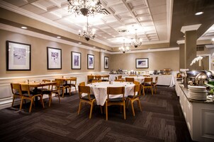 Comedor con mesas y sillas redondas, cuadros en las paredes y una barra para buffet.