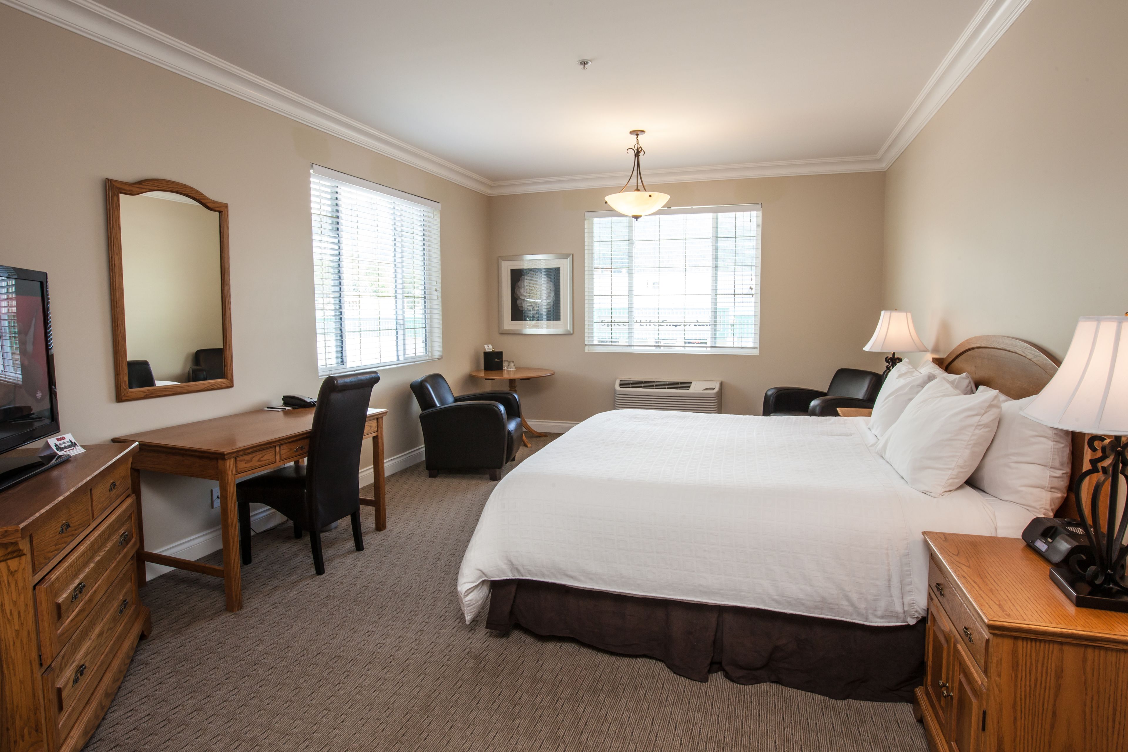 A hotel room with a large bed, a desk, a chair, a television, and a window with blinds.