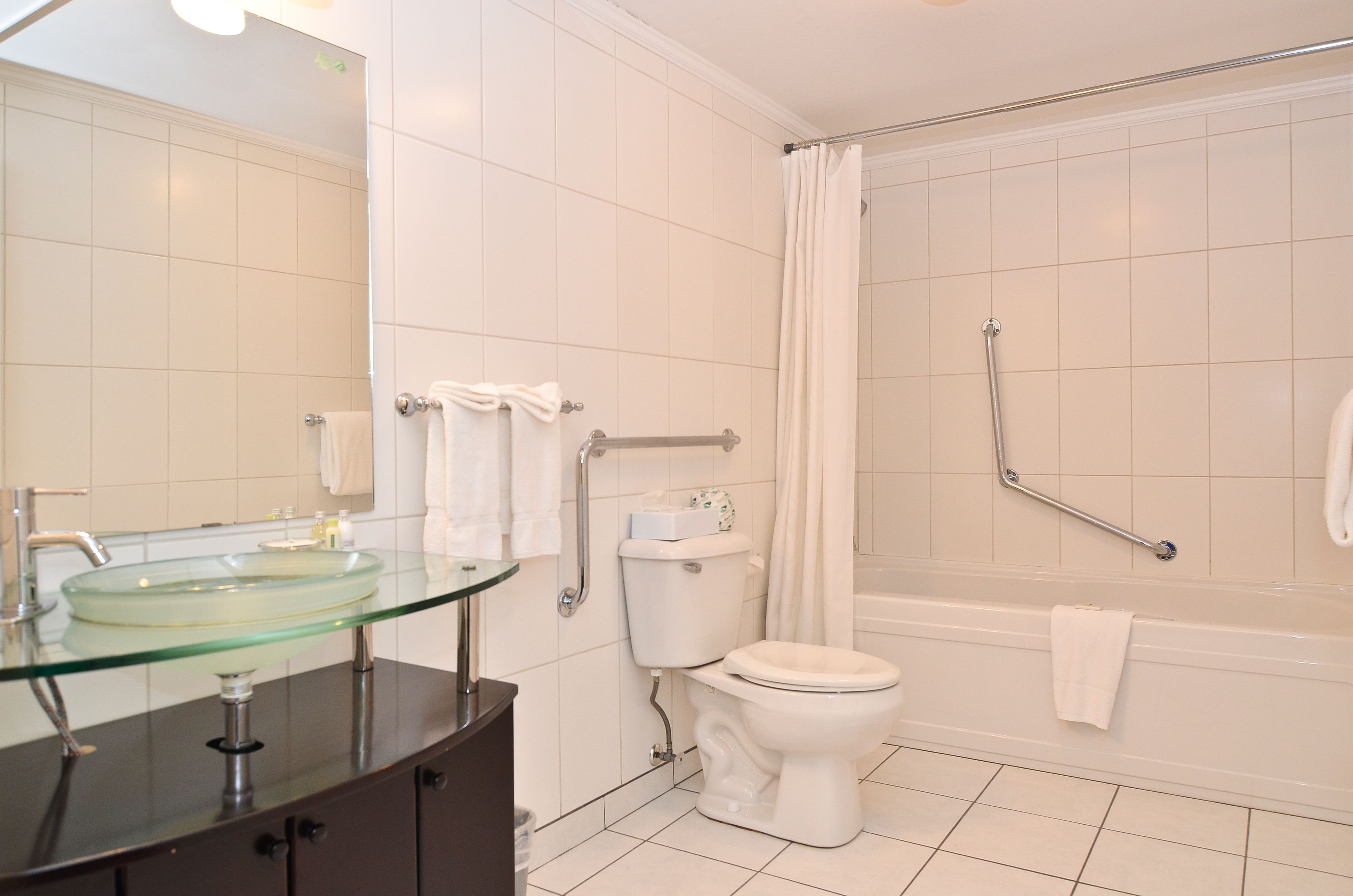 Un baño con lavamanos de vidrio, inodoro blanco y cabina de ducha con barra de apoyo.