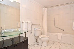 Un baño con lavamanos de vidrio, inodoro blanco y cabina de ducha con barra de apoyo.