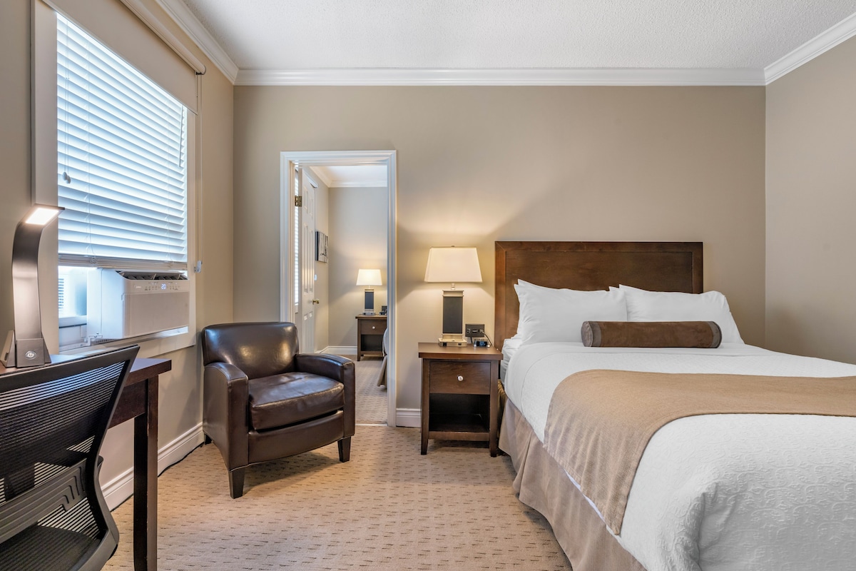 Habitación de hotel con cama, escritorio, silla, mesita de noche y lámpara.