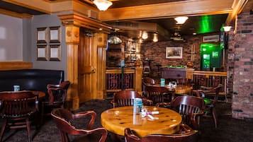A bar area with wooden furniture, a billiards table, and a green machine, likely a cash register or point of sale system.