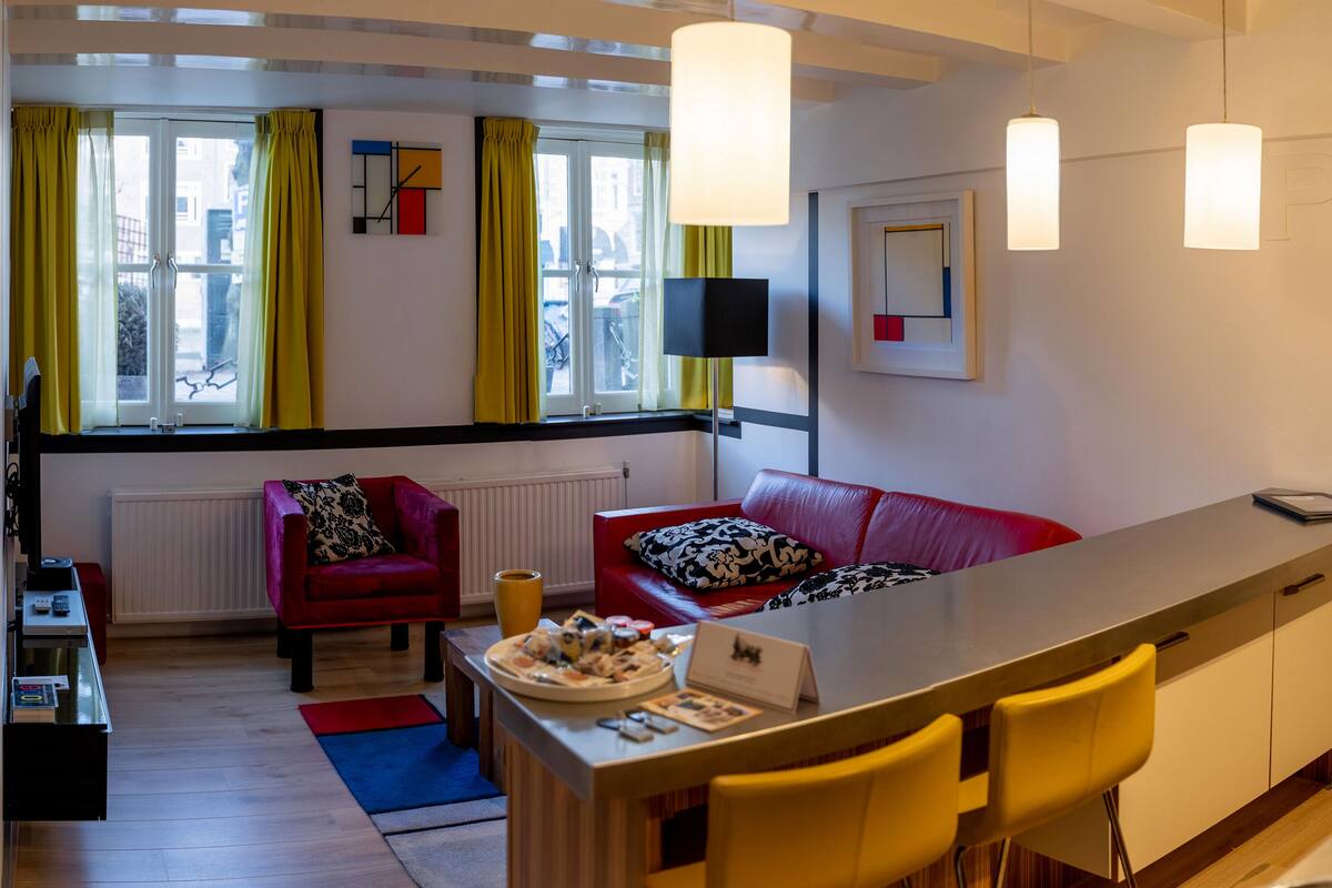 Una sala de estar moderna con un sofá rojo, sillas amarillas, una mesa de comedor con comida y un televisor en la pared.
