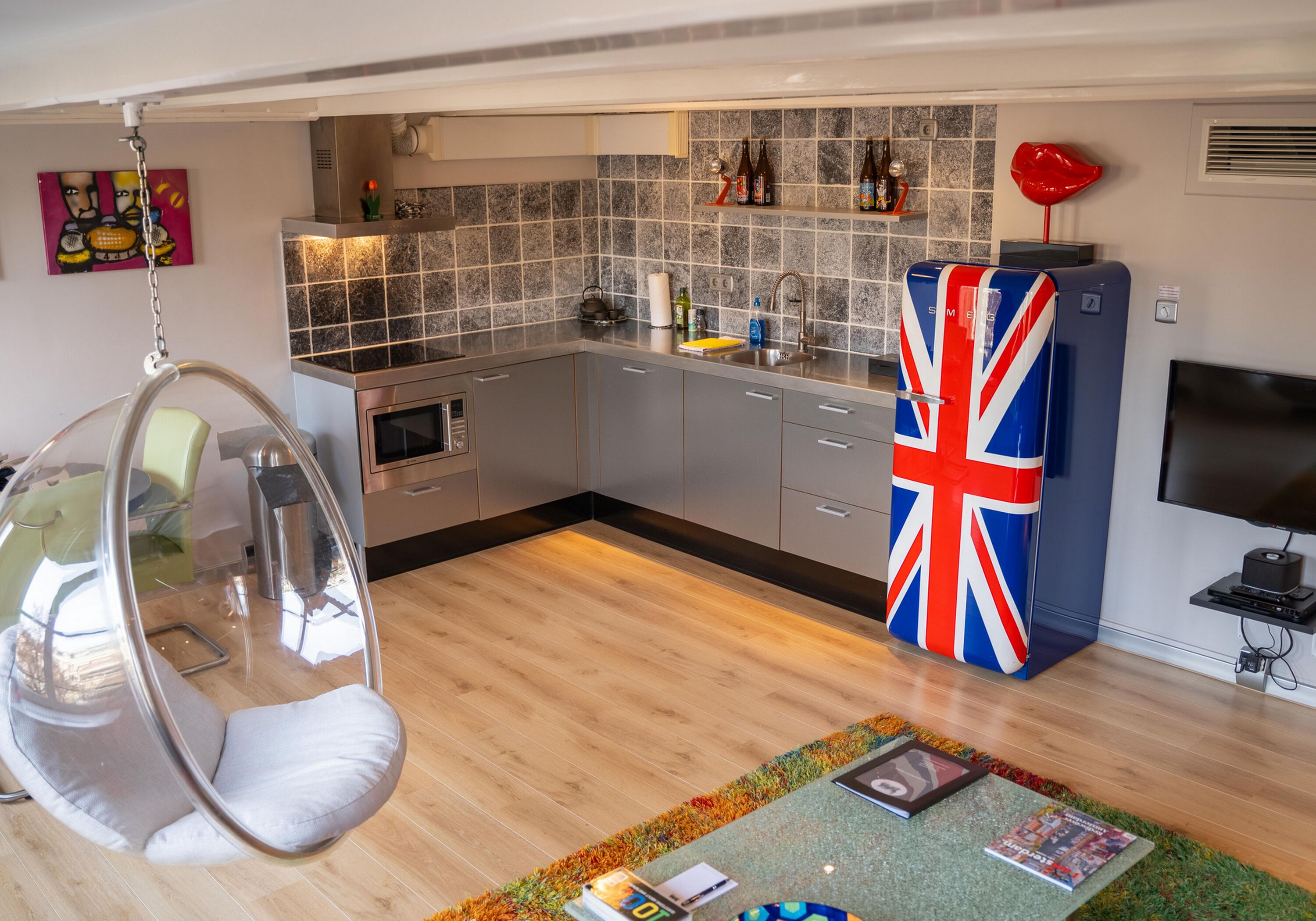 Una cocina moderna con armarios grises, un sillón colgante, un televisor y una bandera del Reino Unido en el refrigerador.