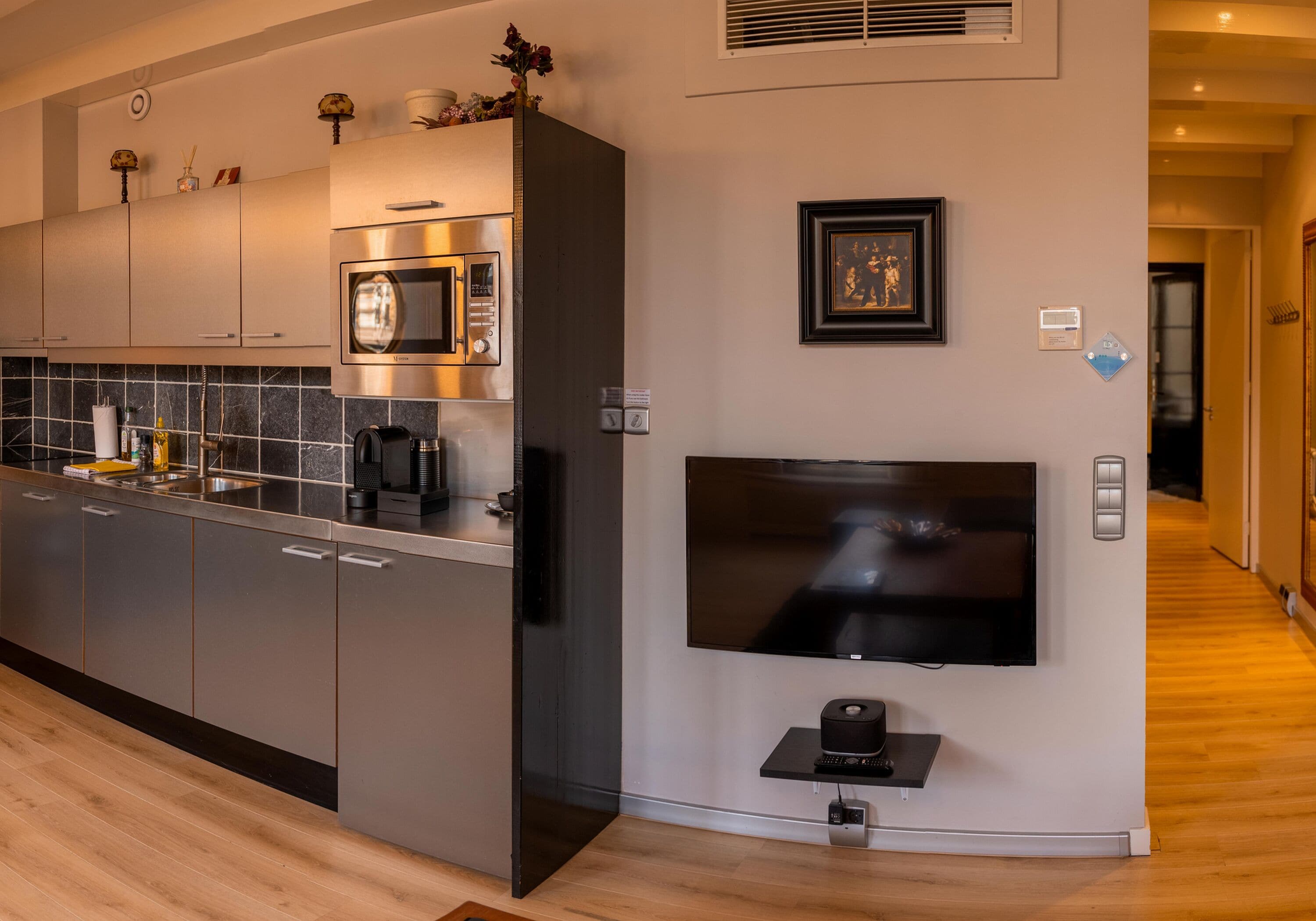 Eine moderne Küche mit Edelstahlgeräten, einem flachbildfernseher an der Wand und Holzboden.