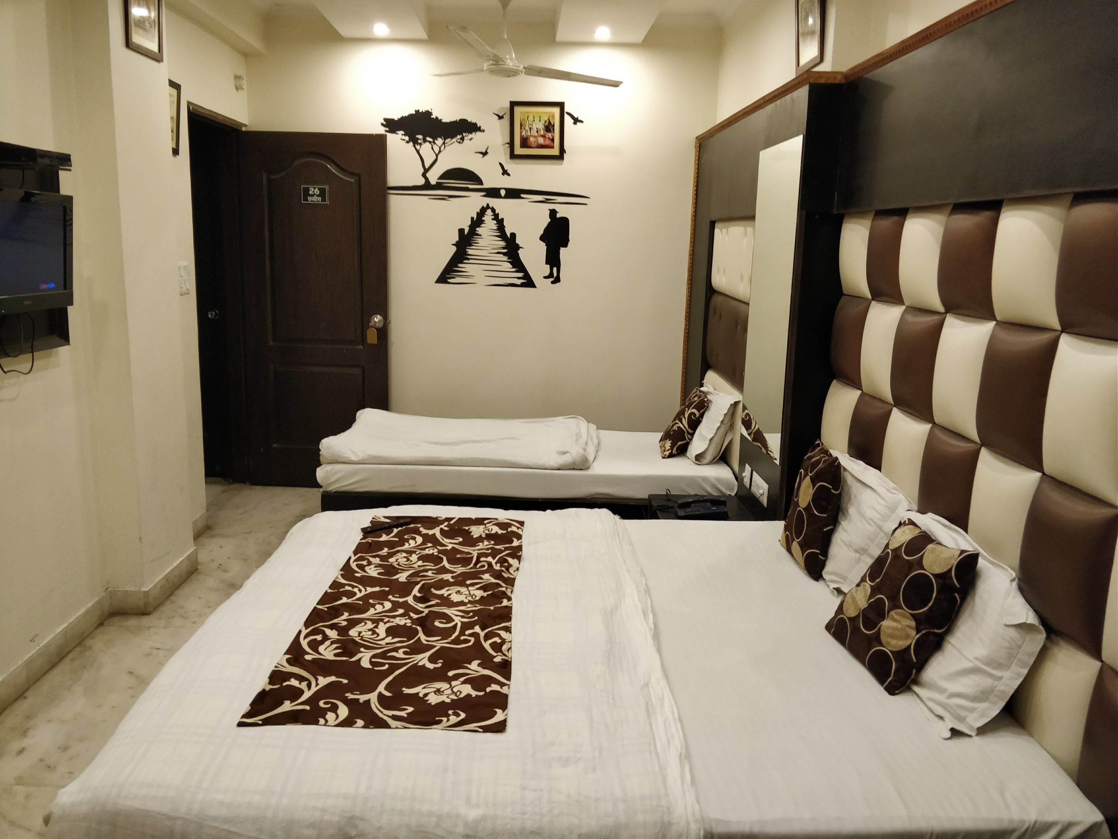 A hotel room with a large bed, a smaller bed, a TV, a ceiling fan, and a door with a number sign.