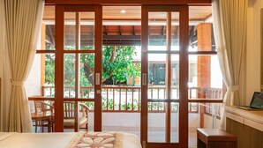A bedroom with a bed, a desk, and a view of a balcony with plants. - Bali Summer Hotel (Kuta)