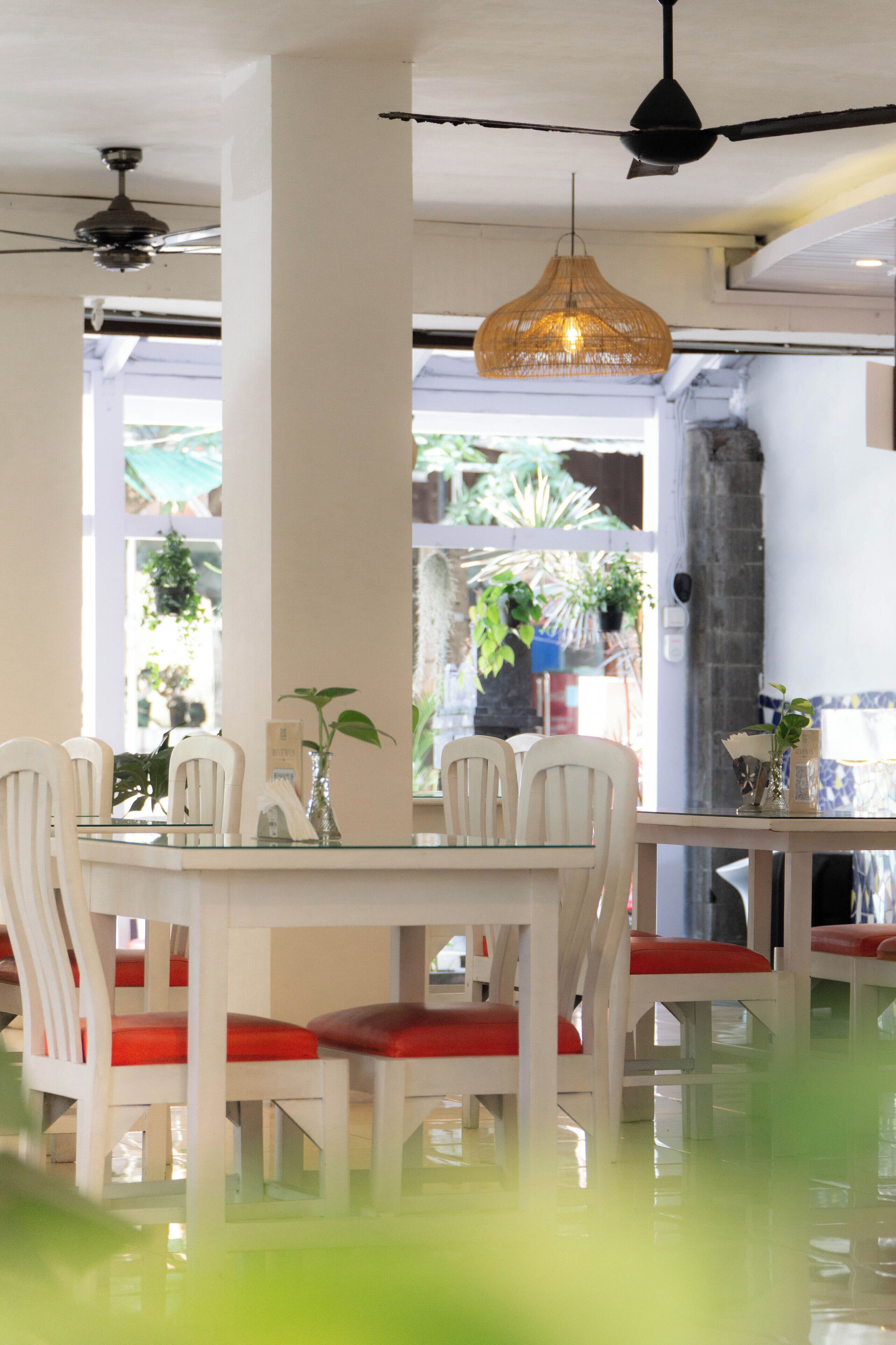 A dining area with white chairs and red cushions, a glass table, and a hanging light fixture.