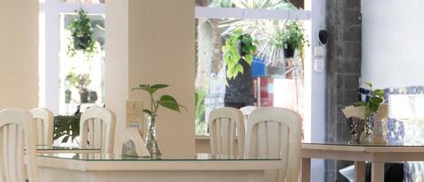 A dining area with white chairs and red cushions, a glass table, and a hanging light fixture.