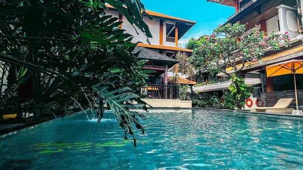 A swimming pool surrounded by tropical plants and a building with a tiled roof. - Bali Summer Hotel (Kuta)