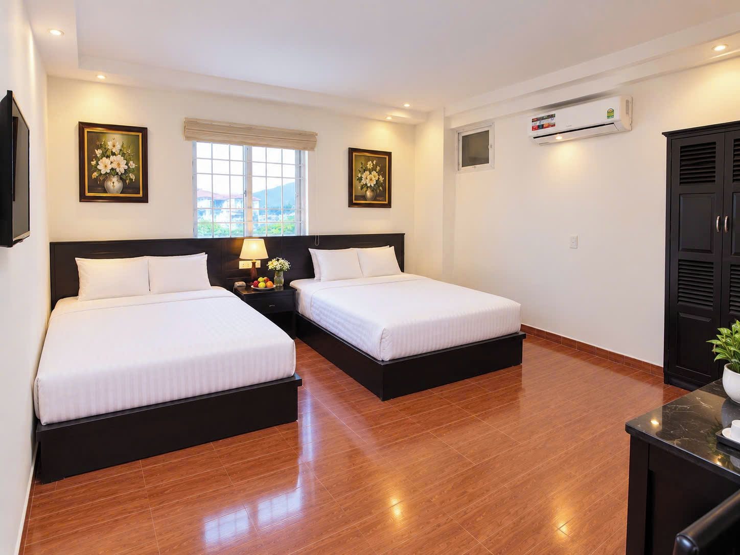 Habitación de hotel con dos camas, una mesita de noche con lámpara, ventana con vistas, equipo de aire acondicionado y armario.