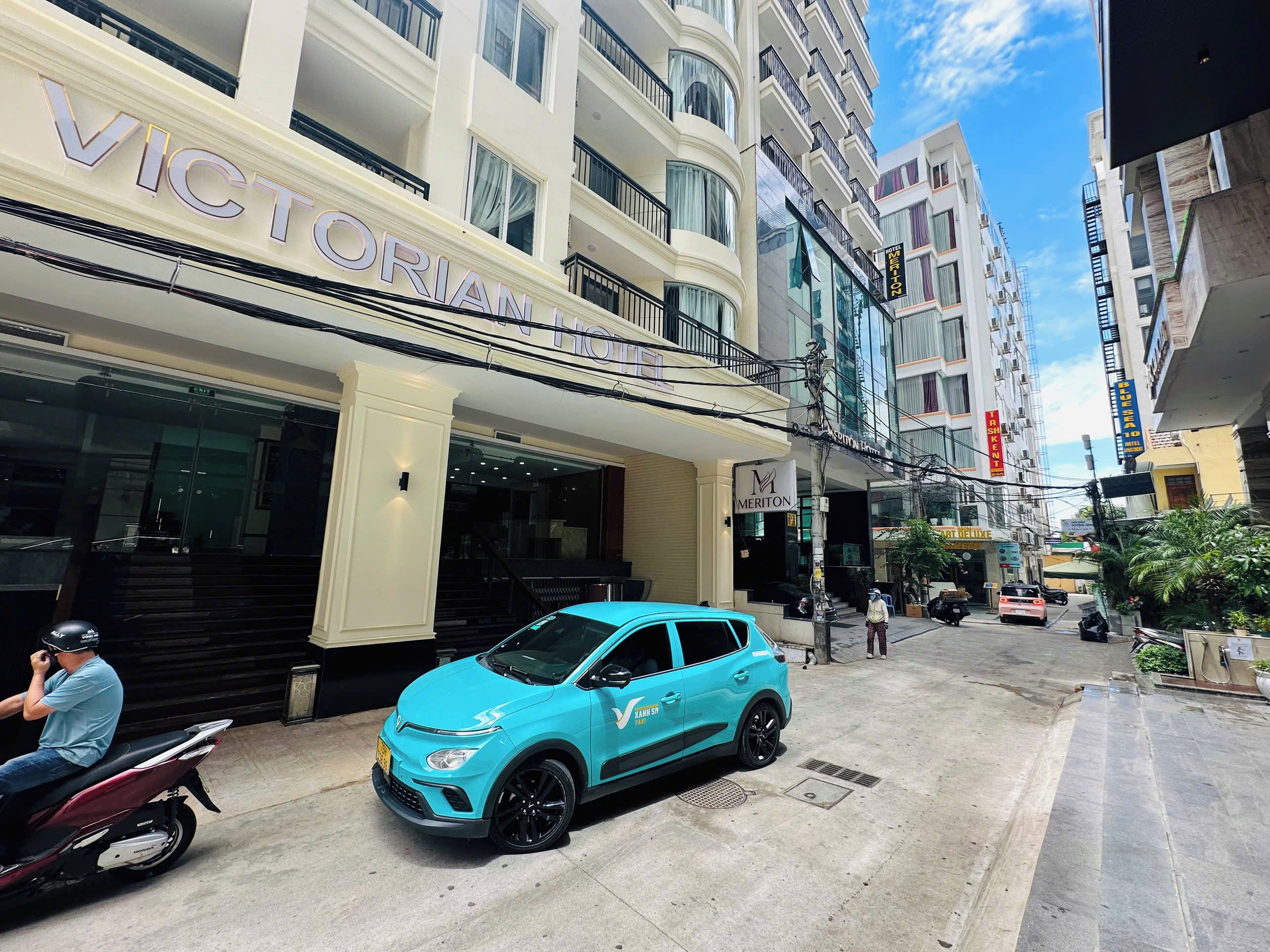 Un hôtel avec une entrée imposante, une voiture bleue garée devant et un trottoir pour les piétons.
