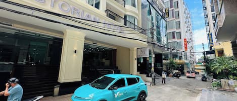 Un hôtel avec une entrée imposante, une voiture bleue garée devant et un trottoir pour les piétons.