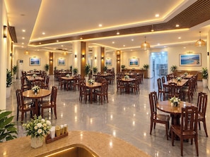 A spacious hotel dining area with multiple tables and chairs, a central reception desk, and a view of the sea through the windows. - Victorian Nha Trang Hotel (Nha Trang)