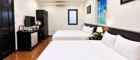 A hotel room with two beds, a desk with a television, and a window with a view of a beach.