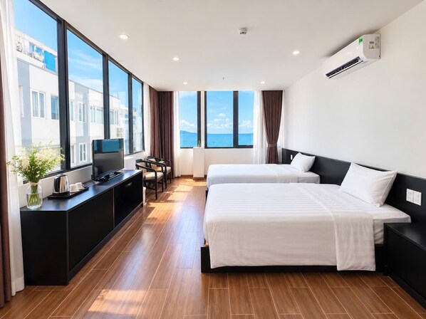 A hotel room with two beds, a TV, a desk with a coffee maker, and a view of the sea. - Victorian Nha Trang Hotel (Nha Trang)