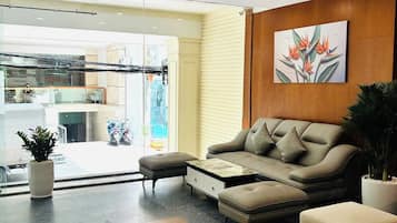 Un hall d’entrée moderne avec un canapé, un pouf et une table basse. On y trouve également une plante en pot et un tapis décoratif.