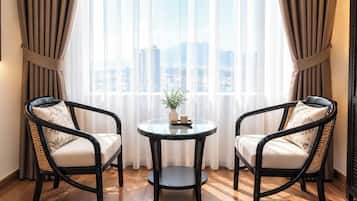 Una habitación con dos sillas de mimbre negro, una mesita redonda y vistas a un paisaje urbano a través de cortinas traslúcidas.
