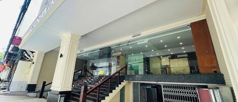 Entrada de un hotel con una escalera que lleva al vestíbulo, una puerta de cristal y una reja metálica.