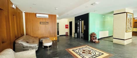 A lobby with a reception desk, a wooden wall, a black elevator, and a patterned floor.