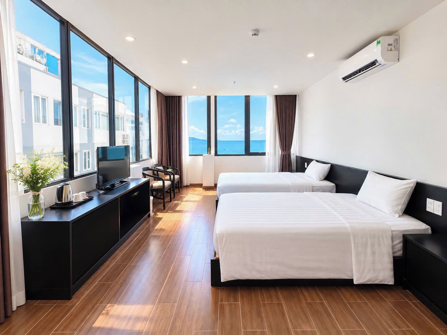 Habitación de hotel con dos camas, televisión, escritorio con cafetera y vista al mar.