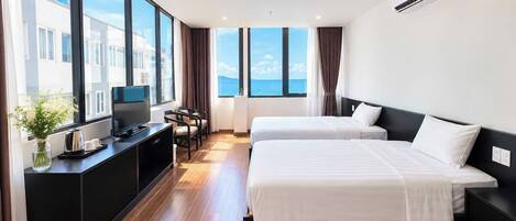 Habitación de hotel con dos camas, televisión, escritorio con cafetera y vista al mar.
