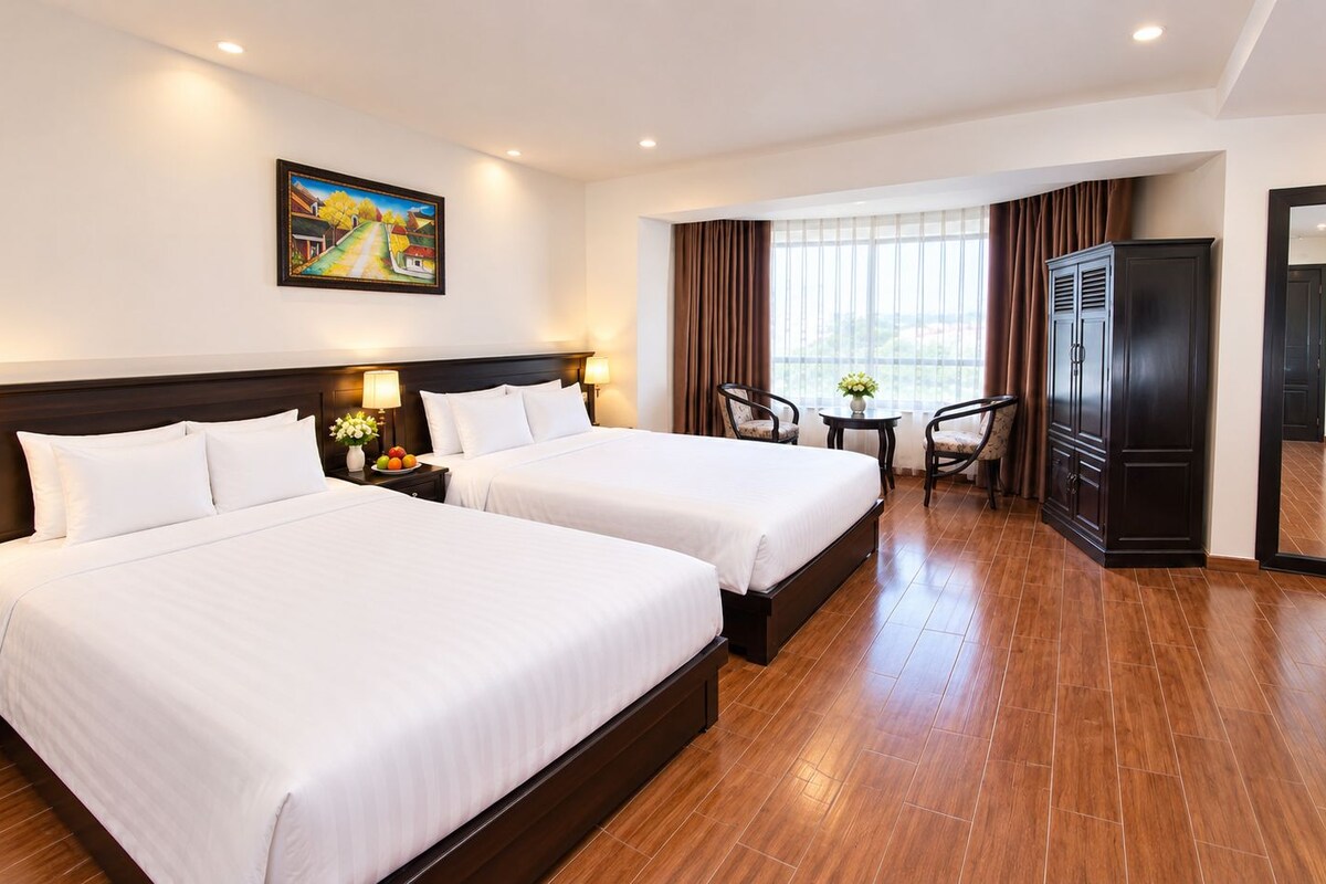 A hotel room with two beds, a desk, a chair, a TV, and a painting on the wall.