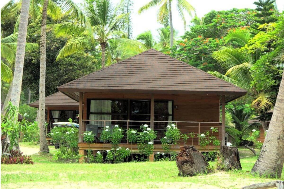 Un bungalow en bois doté d’un toit en pente, entouré d’une végétation luxuriante et de palmiers.