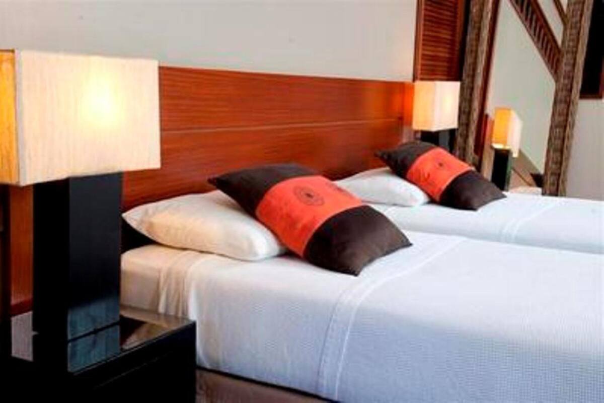 Une chambre d’hôtel avec deux lits, chacun recouvert d’une courtepointe blanche et agrémenté d’oreillers assortis, et dotée d’une tête de lit en bois.