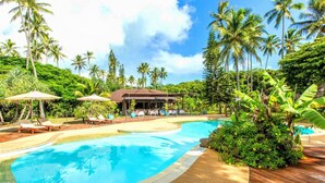 A resort pool area with lounge chairs, umbrellas, and a building with a covered patio.